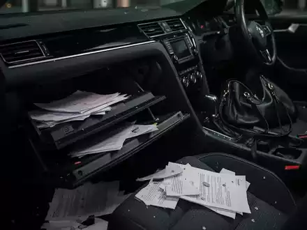 Dunkles Autointerieur mit offenem Handschuhfach und verstreuten Papieren, das einen Diebstahl andeutet. Eine Handtasche fehlt. - Foto: über boerse-global.de
