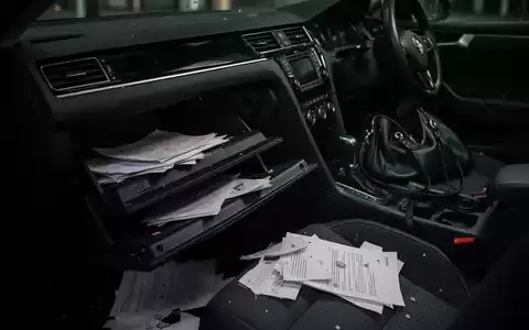 Dunkles Autointerieur mit offenem Handschuhfach und verstreuten Papieren, das einen Diebstahl andeutet. Eine Handtasche fehlt. - Foto: über boerse-global.de