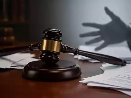 Ein Richterhammer liegt auf einem dunklen Holzschreibtisch, umgeben von verschwommenen Rechtsdokumenten. Eine schemenhafte Hand greift ins Bild. - Foto: über boerse-global.de