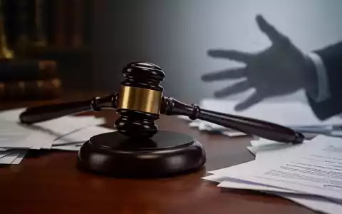 Ein Richterhammer liegt auf einem dunklen Holzschreibtisch, umgeben von verschwommenen Rechtsdokumenten. Eine schemenhafte Hand greift ins Bild. - Foto: über boerse-global.de
