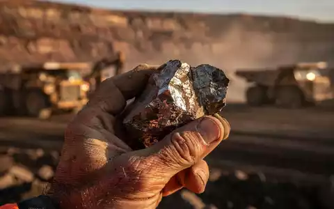 Nahaufnahme einer Hand, die ein Stück Roherz aus kritischem Metall vor dem Hintergrund von Bergbaumaschinen in Nebraska hält. - Foto: über boerse-global.de