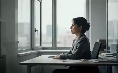 Eine Person sitzt nachdenklich an einem Schreibtisch in einem ruhigen Büro und blickt aus einem Fenster, um Entschleunigung zu signalisieren. - Foto: über boerse-global.de
