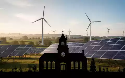 Eine Windturbine und Solarpaneele in einer ländlichen Landschaft mit der Silhouette eines Rathauses im Vordergrund. - Foto: über boerse-global.de