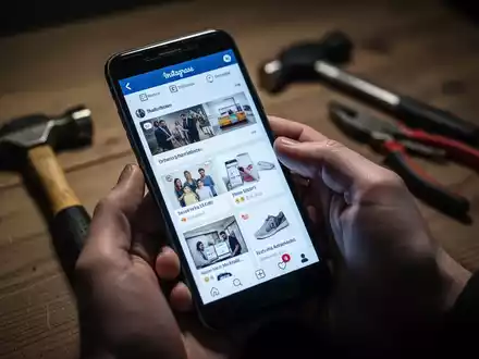 Eine Hand hält ein Smartphone, im Hintergrund verschwommen ein Hammer und eine Zange auf einem Tisch. - Foto: über boerse-global.de