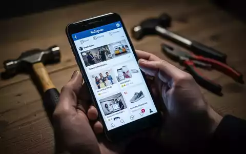 Eine Hand hält ein Smartphone, im Hintergrund verschwommen ein Hammer und eine Zange auf einem Tisch. - Foto: über boerse-global.de