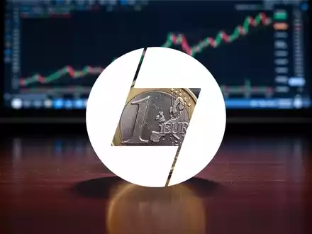 Eine einzelne Euro-Münze steht aufrecht auf einem dunklen Holztisch, im Hintergrund unscharfe Finanzcharts auf einem Bildschirm. - Foto: über boerse-global.de