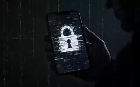 Eine Hand hält ein Smartphone mit einem verzerrten, glitchigen Schloss-Symbol auf dem Bildschirm, das Cyberbedrohungen darstellt. - Foto: über boerse-global.de
