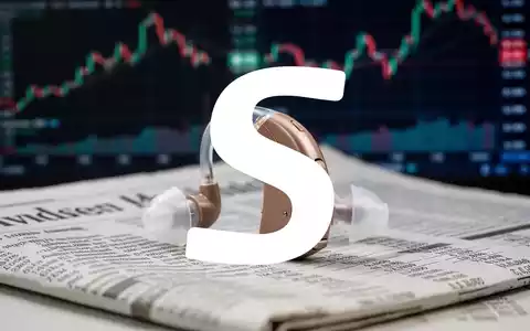 Ein modernes Hörgerät liegt auf einer Finanzzeitung mit unscharfen Börsencharts im Hintergrund. - Foto: über boerse-global.de