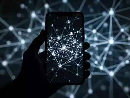 Eine dunkle, stilisierte Hand hält ein Smartphone, dessen Bildschirm mit abstrakten, vernetzten Linien und Knoten leuchtet, die ein Botnet symbolisieren. - Foto: über boerse-global.de
