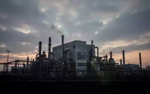 Silhouette einer großen, modernen Fabrik vor einem dramatischen, bewölkten Himmel bei Sonnenuntergang, die wirtschaftliche Unsicherheit und Massenentlassungen darstellt. - Foto: über boerse-global.de