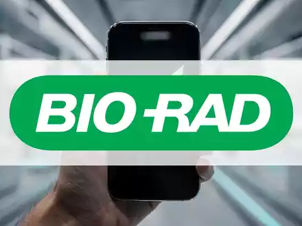 Eine Hand hält ein Smartphone mit einer Börsenhandels-App, die einen grünen, steigenden Graphen zeigt, im Hintergrund eine biotechnische Anlage. - Foto: über boerse-global.de
