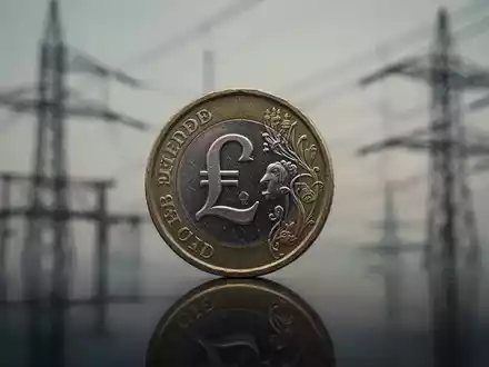 Eine britische Pfundmünze im Vordergrund, im Hintergrund verschwommene Stromleitungen und Versorgungsinfrastruktur. - Foto: über boerse-global.de