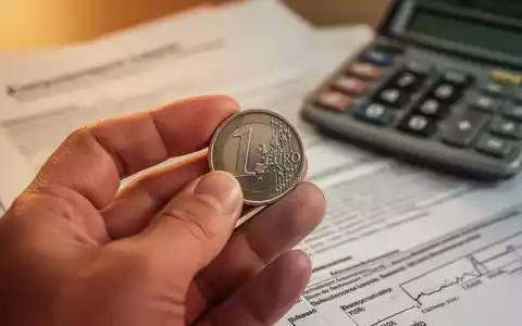 Nahaufnahme einer Hand, die eine deutsche Euro-Münze hält, mit verschwommenen juristischen Dokumenten und einem Taschenrechner im Hintergrund. - Foto: über boerse-global.de