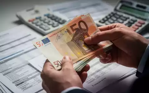 Hände zählen einen 50-Euro-Schein, im Hintergrund sind unscharfe Finanzdokumente und ein Taschenrechner zu sehen. - Foto: über boerse-global.de