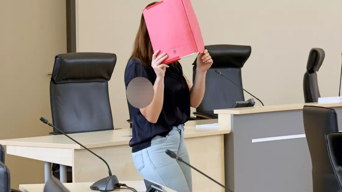 Die Angeklagte betritt den Gerichtssaal mit rotem Aktendeckel vor dem Gesicht. - Bild: A7120 Bernd Wüstneck/dpa