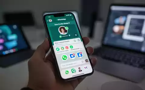 Eine Hand hält ein Smartphone mit der WhatsApp-App, die neue Funktionen für Status und Kontoverwaltung zeigt. Im Hintergrund sind weitere digitale Geräte verschwommen. - Foto: über boerse-global.de