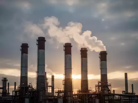 Industrieschornsteine emittieren Dampf oder weißen Rauch, vor einem dramatischen Himmel, der regulatorische Änderungen und wirtschaftliche Auswirkungen symbolisiert. - Foto: über boerse-global.de