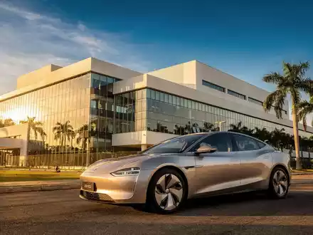 Ein glänzendes BYD Elektrofahrzeug vor einer modernen Fabrik in Brasilien, umgeben von Palmen unter blauem Himmel. - Foto: über boerse-global.de