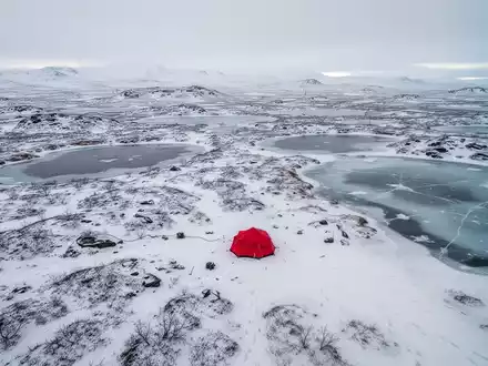 Luftaufnahme einer weiten, schneebedeckten arktischen Landschaft mit einem kleinen roten Zelt, das Rohstoffexploration symbolisiert. - Foto: über boerse-global.de