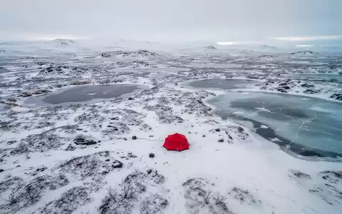 Luftaufnahme einer weiten, schneebedeckten arktischen Landschaft mit einem kleinen roten Zelt, das Rohstoffexploration symbolisiert. - Foto: über boerse-global.de