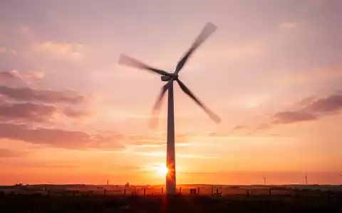 Eine Windkraftanlage bei Sonnenaufgang, ihre Rotorblätter in Bewegung, vor einem farbigen Himmel. - Foto: über boerse-global.de