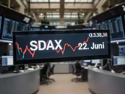 Ein Börsenticker zeigt einen leichten Kursrückgang mit dem Text 'SDAX' und '22. Juni', im Hintergrund eine Börse. - Foto: über boerse-global.de