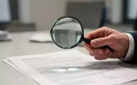 Eine Nahaufnahme einer Hand, die eine Lupe über ein Dokument mit verschwommenem Text hält, symbolisiert Datenschutz und Compliance. - Foto: über boerse-global.de