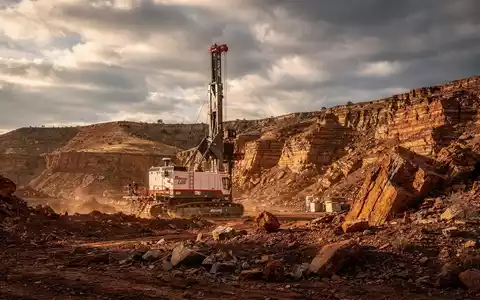 Eine geologische Bohranlage in einer rauen Landschaft unter dramatischem Himmel, mit kupferfarbenen Gesteinsformationen. - Foto: über boerse-global.de