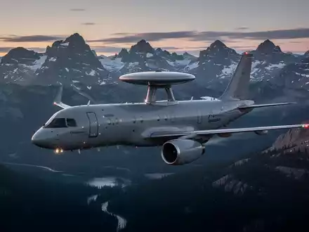 Ein modernes AEW&C-Flugzeug, möglicherweise ein GlobalEye, fliegt bei Sonnenuntergang über eine raue kanadische Landschaft. - Foto: über boerse-global.de