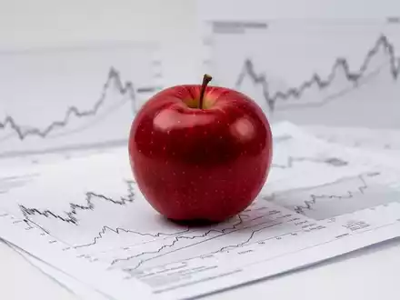 Ein roter Apfel auf einem Finanzbericht mit unscharfen Börsencharts im Hintergrund, symbolisiert Konsumgüter und Marktanalyse. - Foto: über boerse-global.de
