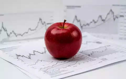 Ein roter Apfel auf einem Finanzbericht mit unscharfen Börsencharts im Hintergrund, symbolisiert Konsumgüter und Marktanalyse. - Foto: über boerse-global.de