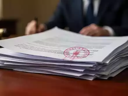 Nahaufnahme von juristischen Dokumenten auf einem Holztisch mit einem roten Stempel. Eine unscharfe Person ist im Hintergrund zu sehen. - Foto: über boerse-global.de