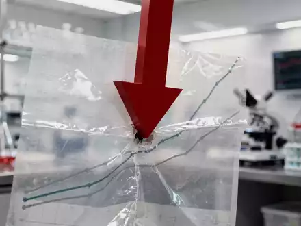 Ein roter, stark abwärts gerichteter Börsenpfeil durchbohrt einen transparenten Chart vor einem verschwommenen Laborhintergrund. - Foto: über boerse-global.de