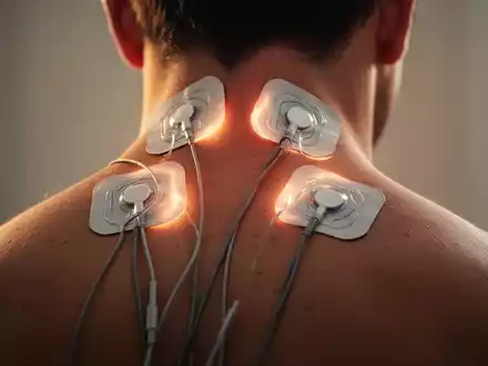 Nahaufnahme des oberen Rückens und Nackens einer Person mit TENS-Elektroden, die sanft leuchten und therapeutische Wärme andeuten. - Foto: über boerse-global.de