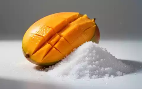 Eine aufgeschnittene, reife Mango neben einem Haufen Zucker, visuell kontrastreich und minimalistisch dargestellt. - Foto: über boerse-global.de