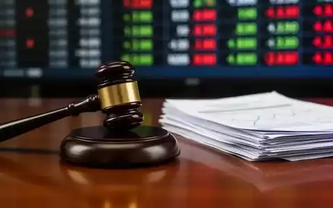 Ein Nahaufnahme eines Holzhammers auf einem Schreibtisch neben Finanzdokumenten, mit einem unscharfen Börsenticker im Hintergrund. - Foto: über boerse-global.de