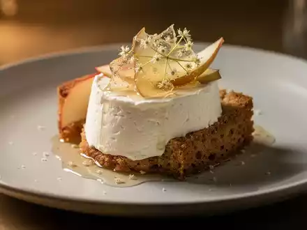 Ein kunstvoll angerichtetes Gourmet-Dessert mit Ziegenfrischkäsemousse, Dattelbrioche und Apfel-Holundergelee auf einem Teller. - Foto: über boerse-global.de