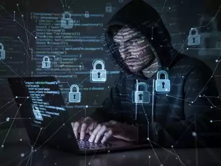 A shadowy figure in a hoodie types on a laptop, with lines of code and digital lock icons overlaid, symbolizing a cyberattack. - Foto: über boerse-global.de