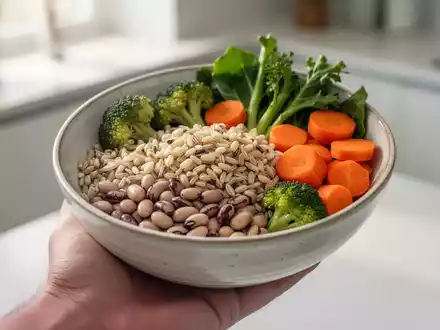 Eine Nahaufnahme einer Hand, die eine Schüssel mit einer ausgewogenen Mahlzeit aus Vollkornprodukten, Hülsenfrüchten und Gemüse hält. - Foto: über boerse-global.de