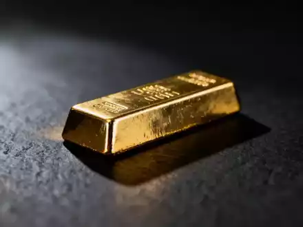 Ein einzelner glänzender Goldbarren ruht auf einer dunklen, texturierten Oberfläche, teilweise im Schatten. - Foto: über boerse-global.de