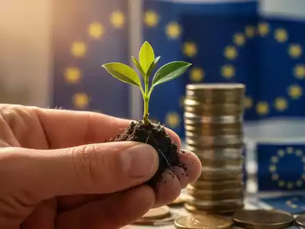 Eine Hand hält einen Pflanzenspross, im Hintergrund unscharf Münzen und EU-Flaggen, die finanzielle Entlastung und Nachhaltigkeit symbolisieren. - Foto: über boerse-global.de