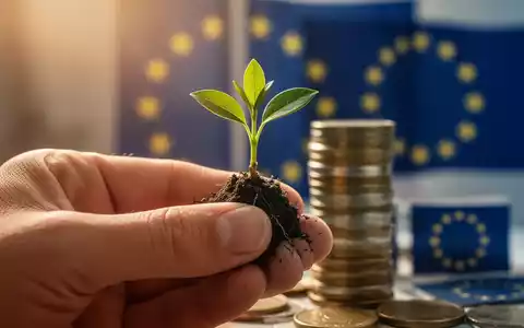 Eine Hand hält einen Pflanzenspross, im Hintergrund unscharf Münzen und EU-Flaggen, die finanzielle Entlastung und Nachhaltigkeit symbolisieren. - Foto: über boerse-global.de