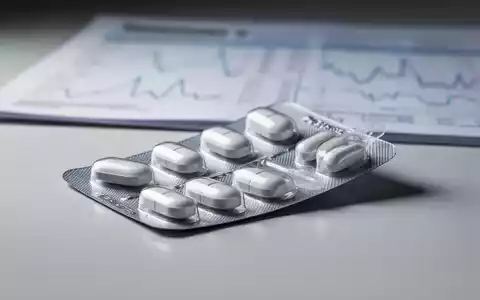 Ein Blisterpack mit weissen ovalen Tabletten, teilweise geöffnet, auf einer reflektierenden Oberfläche. Im Hintergrund unscharfe medizinische Daten. - Foto: über boerse-global.de