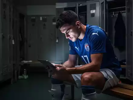 Ein Fußballspieler sitzt nachdenklich in einer Umkleidekabine, symbolisiert mentale Vorbereitung und psychologische Unterstützung im Sport. - Foto: über boerse-global.de