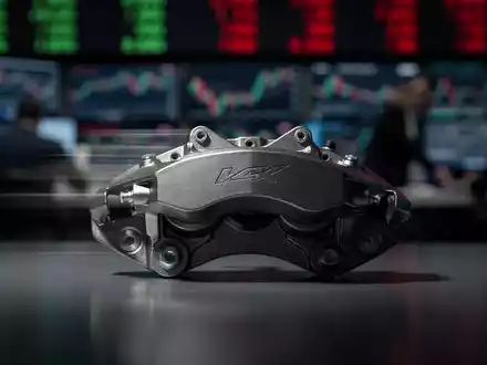 Ein einzelner, glänzender Bremsattel vor einem unscharfen Hintergrund eines Börsenparketts, der eine Verlangsamung andeutet. - Foto: über boerse-global.de