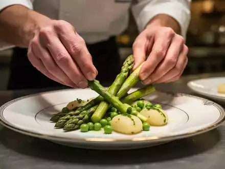 Hände eines Kochs arrangieren kunstvoll grünen Spargel, Erbsen und Gnocchi auf einem Teller in einem gehobenen Restaurant. - Foto: über boerse-global.de