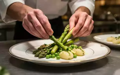 Hände eines Kochs arrangieren kunstvoll grünen Spargel, Erbsen und Gnocchi auf einem Teller in einem gehobenen Restaurant. - Foto: über boerse-global.de
