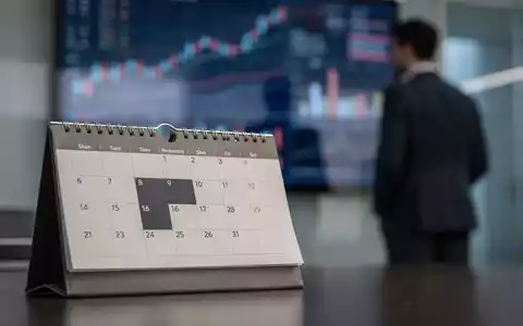 Ein Kalender mit dem Datum 12. November, im Hintergrund eine Person, die Finanzdiagramme betrachtet. - Foto: über boerse-global.de