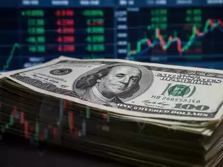 Ein Stapel Dollarnoten mit einer unscharfen Darstellung von Finanzdaten im Hintergrund, die auf den Rohstoffmarkt hindeuten. - Foto: über boerse-global.de