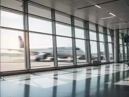 Ein modernes, helles Flughafenterminal mit großen Fenstern und einem unscharfen Flugzeug im Hintergrund. - Foto: über boerse-global.de